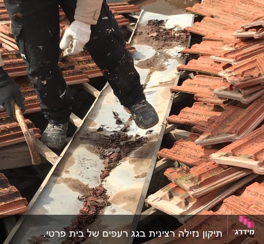 אדם מנקה תעלה על גג רעפים עם כלי עבודה